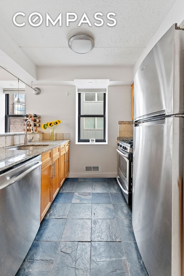 kitchen featuring baseboards, visible vents, appliances with stainless steel finishes, light stone countertops, and a sink