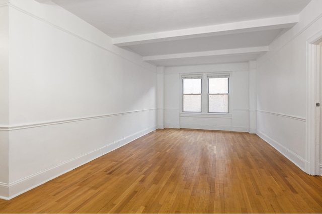 unfurnished room with baseboards, beamed ceiling, and light wood finished floors