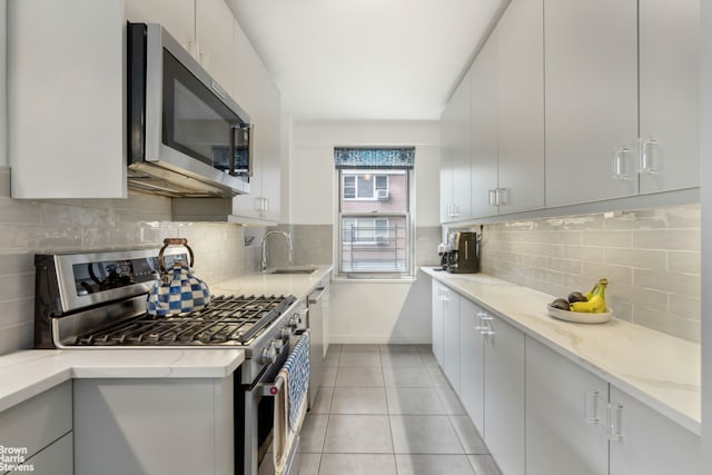 kitchen featuring a sink, light stone countertops, stainless steel appliances, backsplash, and light tile patterned flooring