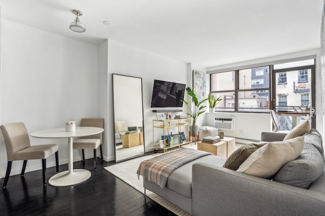 living area featuring wood finished floors, a baseboard heating unit, baseboards, and a wall mounted air conditioner