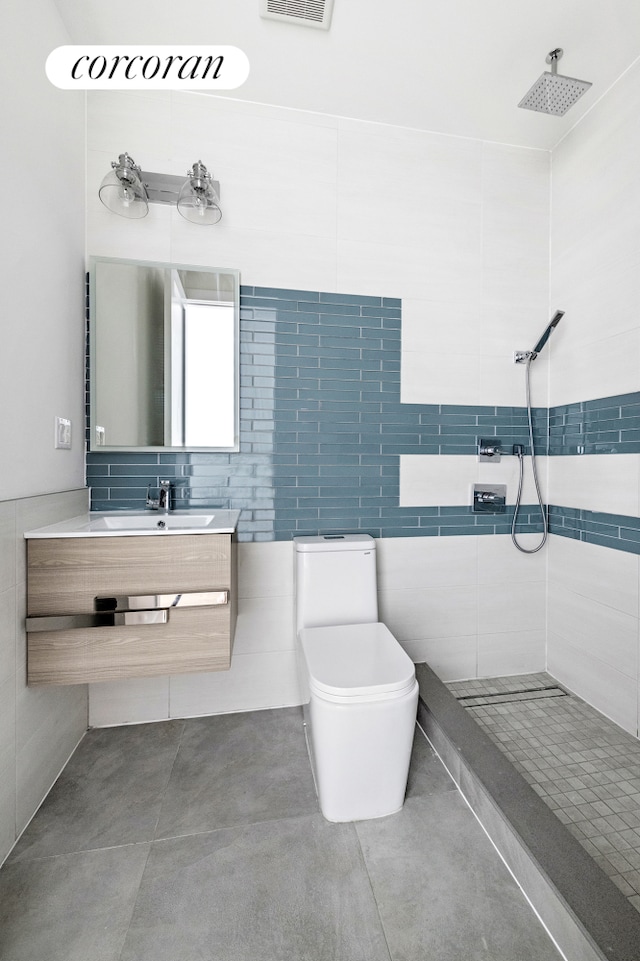 bathroom featuring visible vents, tile walls, toilet, a tile shower, and vanity