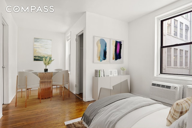 bedroom with an AC wall unit, multiple windows, wood finished floors, and baseboards