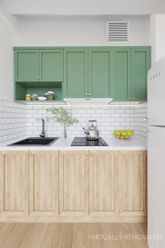 kitchen with black electric stovetop, a sink, visible vents, green cabinets, and freestanding refrigerator