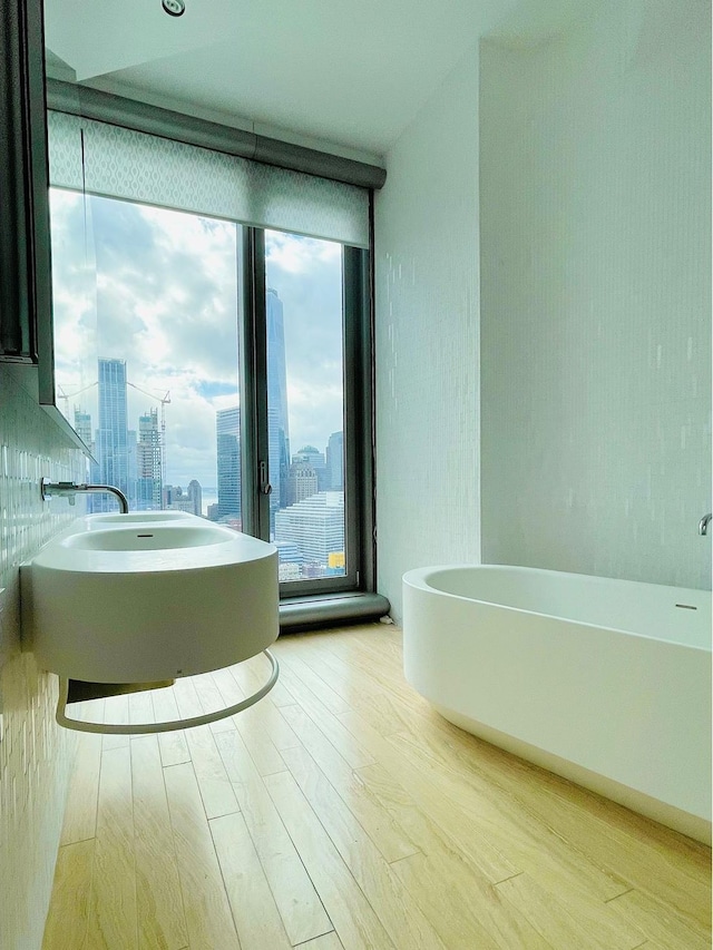 bathroom with expansive windows, a soaking tub, a city view, and wood finished floors