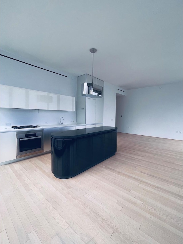 kitchen with light wood-style floors, pendant lighting, oven, and gas cooktop