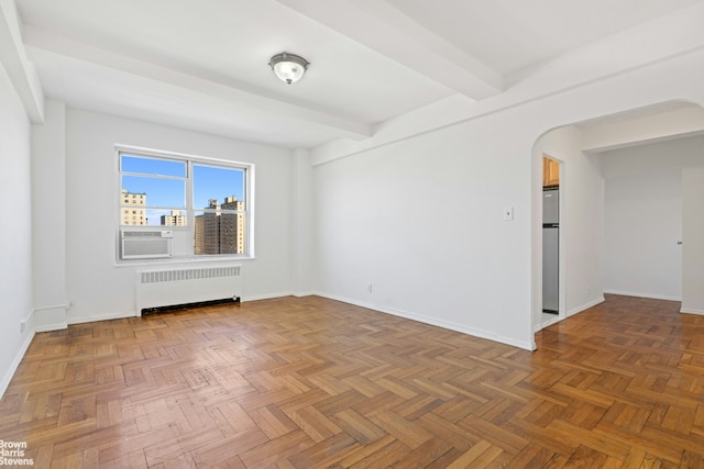 empty room featuring beam ceiling, baseboards, arched walkways, and radiator