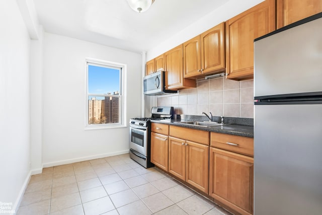 kitchen with decorative backsplash, baseboards, appliances with stainless steel finishes, and a sink