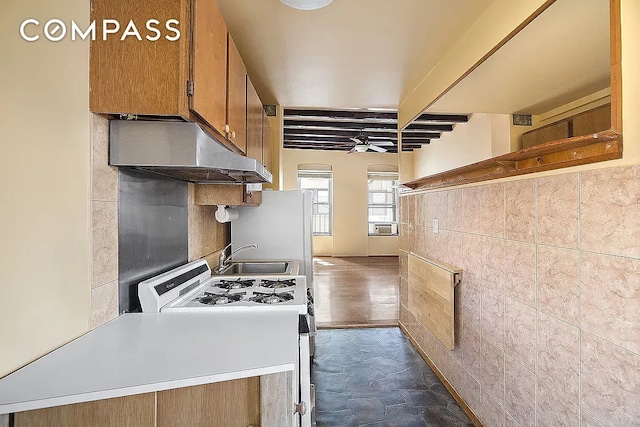 kitchen featuring range with gas stovetop, brown cabinetry, a sink, under cabinet range hood, and stone finish flooring