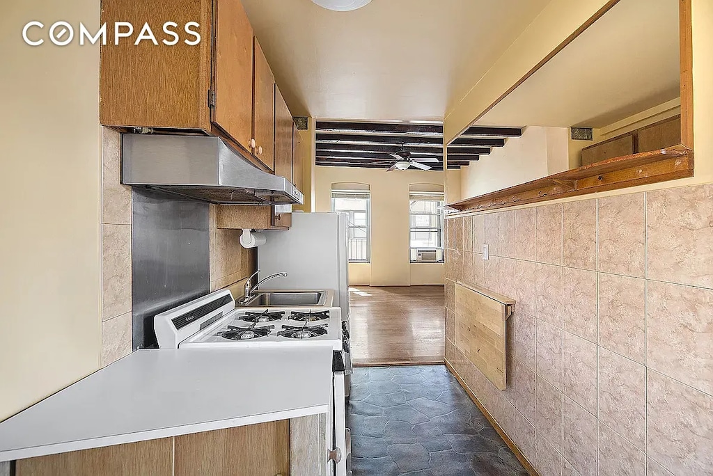 kitchen featuring range with gas stovetop, beamed ceiling, under cabinet range hood, brown cabinets, and a sink