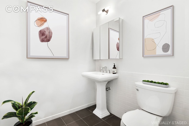 bathroom with a wainscoted wall, tile patterned flooring, toilet, and tile walls