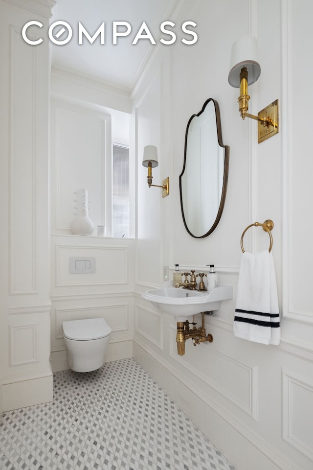 half bathroom with a sink, toilet, a decorative wall, and crown molding