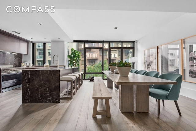 dining space featuring light wood finished floors, visible vents, and a wall of windows