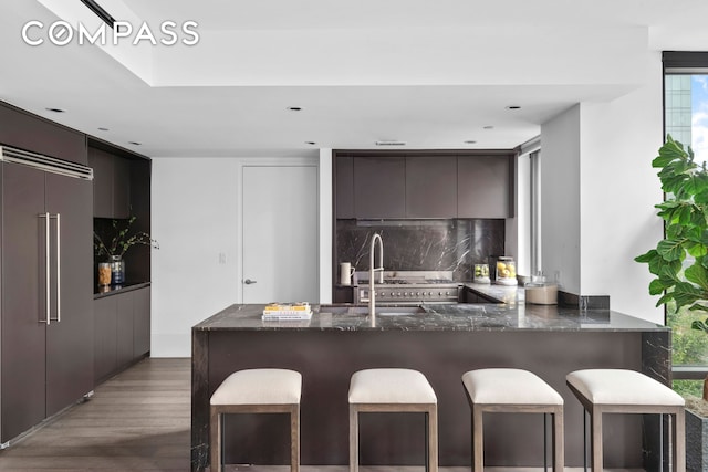 kitchen featuring paneled refrigerator, a peninsula, a kitchen breakfast bar, tasteful backsplash, and modern cabinets