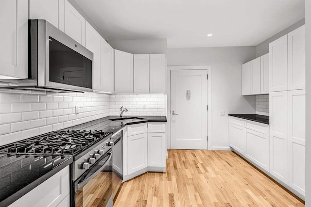 kitchen featuring light wood-type flooring, appliances with stainless steel finishes, white cabinets, and a sink