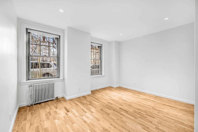 unfurnished room featuring light wood-style floors, radiator, and baseboards