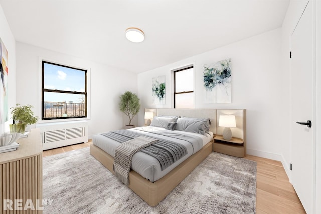 bedroom featuring multiple windows, radiator, light wood-style flooring, and baseboards