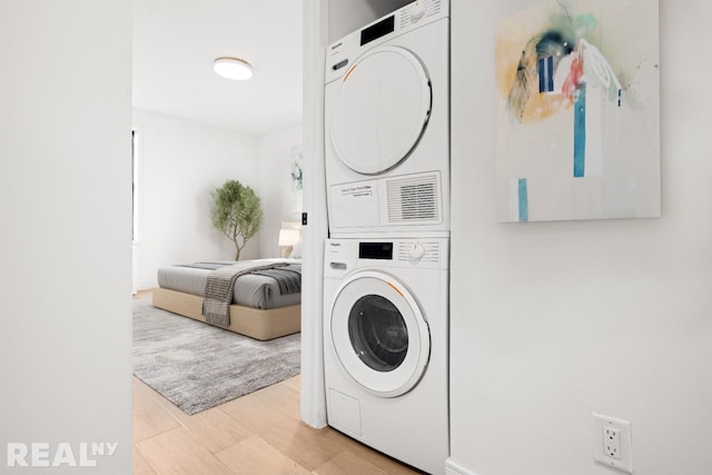 clothes washing area featuring stacked washer and clothes dryer and light wood finished floors
