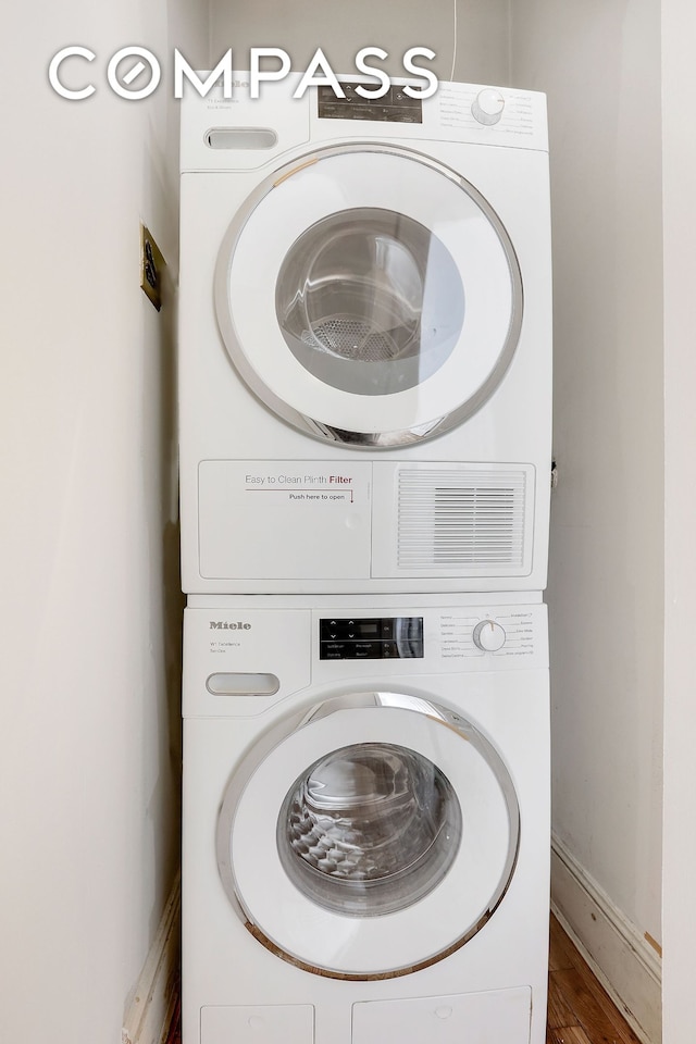 laundry area featuring wood finished floors, stacked washer and clothes dryer, baseboards, and laundry area