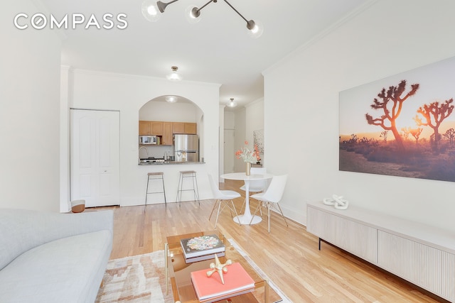 living area featuring arched walkways, ornamental molding, light wood-type flooring, and baseboards