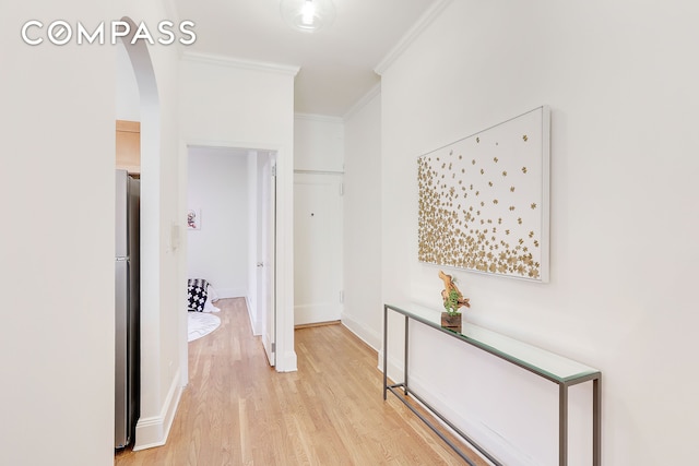 hallway featuring ornamental molding, arched walkways, light wood-style floors, and baseboards