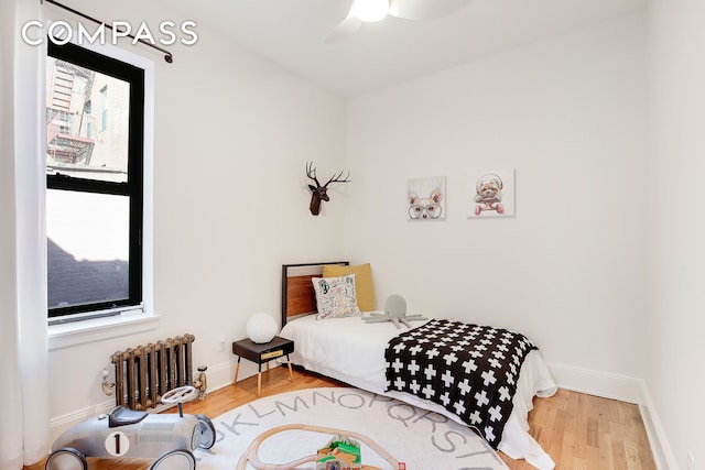 bedroom featuring radiator heating unit, baseboards, ceiling fan, and wood finished floors