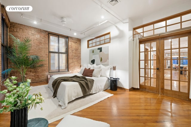 bedroom featuring french doors, visible vents, brick wall, and wood finished floors