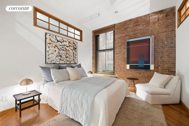 bedroom with brick wall, visible vents, and wood finished floors