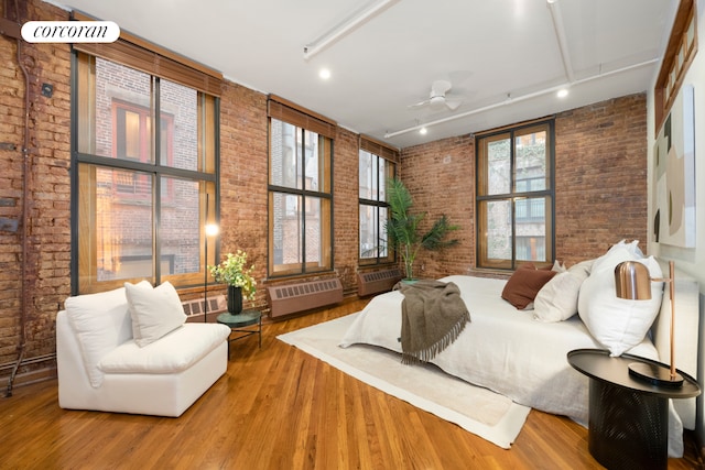 bedroom with a towering ceiling, brick wall, and wood finished floors