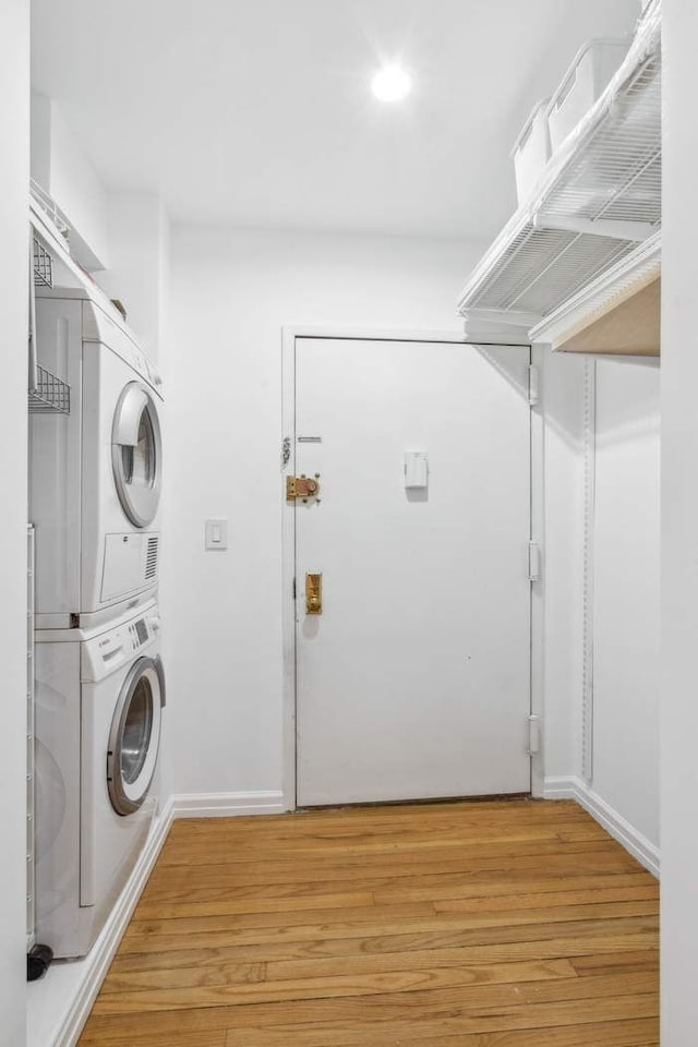 laundry room with stacked washer and dryer, baseboards, light wood finished floors, and laundry area