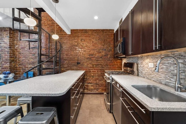 kitchen featuring brick wall, appliances with stainless steel finishes, a sink, and dark brown cabinetry