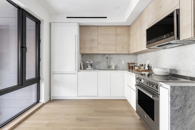 kitchen with tasteful backsplash, modern cabinets, stainless steel appliances, light wood-type flooring, and a sink