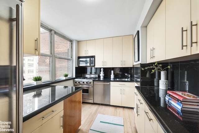 kitchen with decorative backsplash, dark stone counters, appliances with stainless steel finishes, light wood-style floors, and a sink