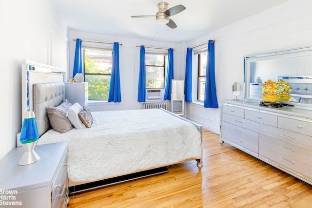 bedroom with light wood-type flooring, ceiling fan, radiator, and cooling unit