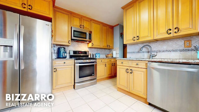 kitchen featuring light tile patterned floors, light stone counters, a sink, appliances with stainless steel finishes, and backsplash