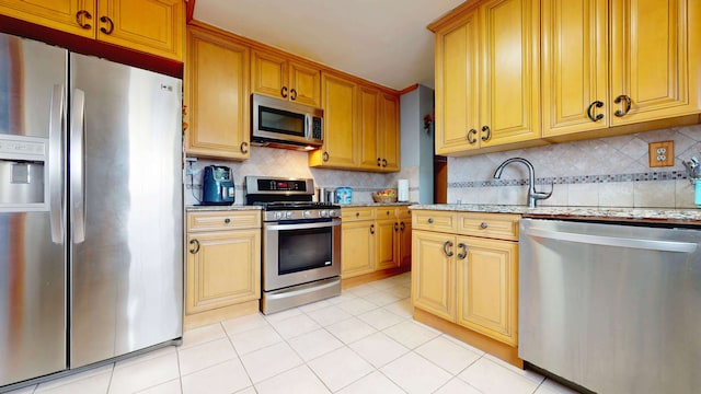 kitchen with light tile patterned floors, appliances with stainless steel finishes, light stone counters, and backsplash