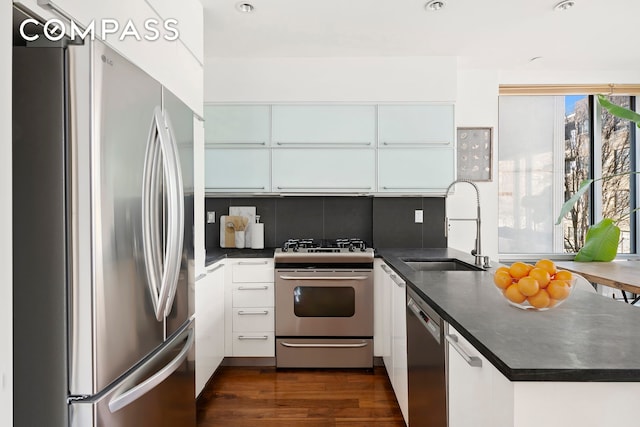 kitchen with appliances with stainless steel finishes, dark countertops, a sink, and dark wood finished floors