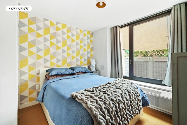 bedroom featuring access to exterior, an accent wall, baseboards, and wood finished floors