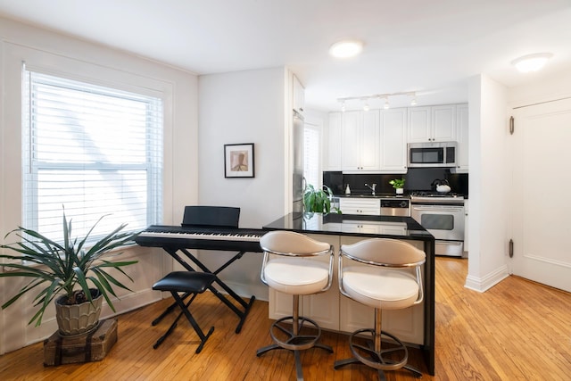 kitchen with a breakfast bar, stainless steel appliances, white cabinetry, dark countertops, and light wood-type flooring