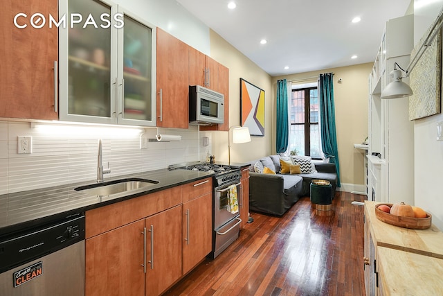 kitchen featuring stainless steel appliances, dark wood-type flooring, a sink, backsplash, and glass insert cabinets