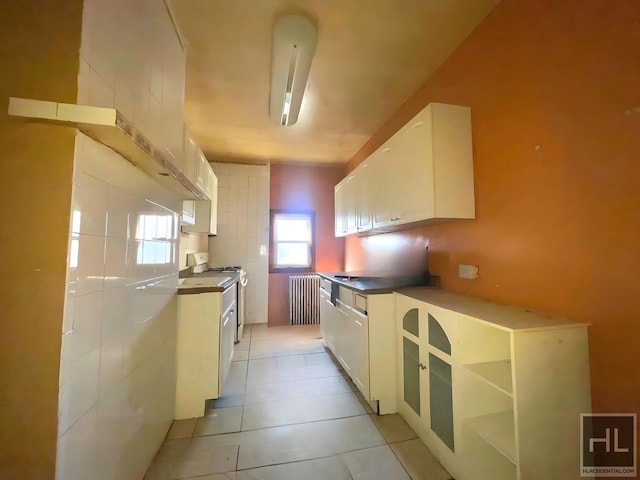 kitchen featuring tasteful backsplash, radiator, gas range gas stove, light tile patterned floors, and white cabinets