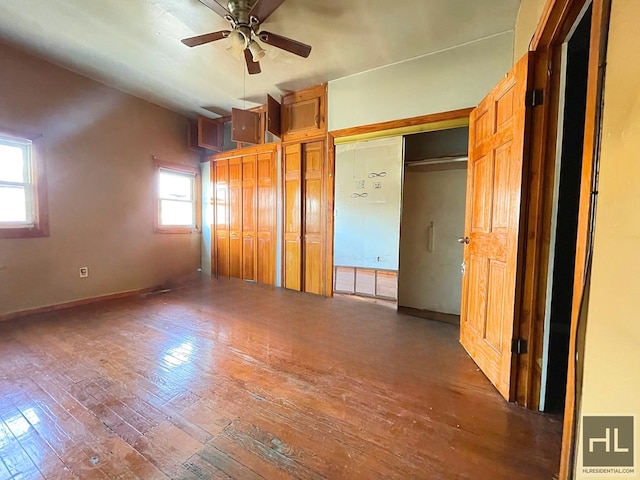 unfurnished bedroom with baseboards, wood-type flooring, a ceiling fan, and multiple closets