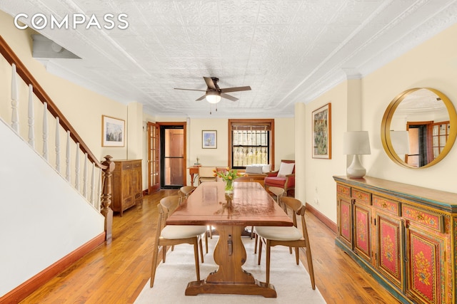 dining space with light wood-style flooring, a ceiling fan, baseboards, stairway, and crown molding