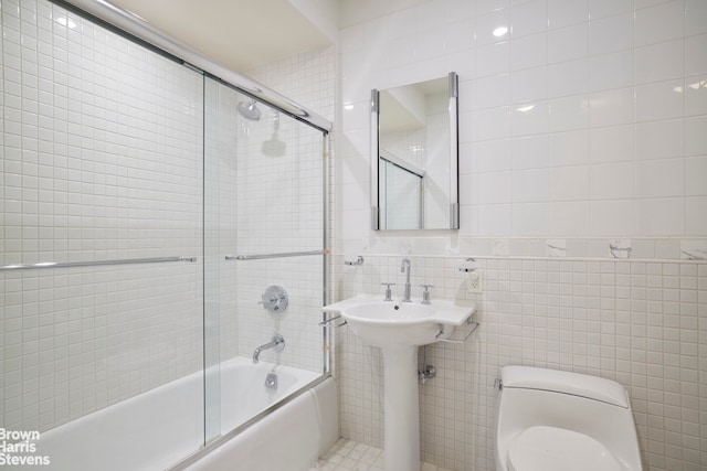 bathroom featuring toilet, shower / bath combination with glass door, and tile walls