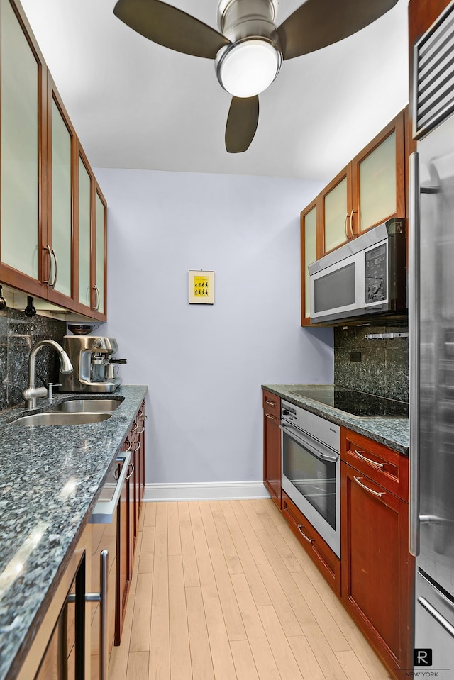 kitchen featuring a sink, dark stone counters, stainless steel appliances, a ceiling fan, and backsplash