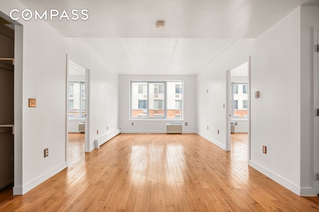 unfurnished living room with baseboard heating, light wood-style floors, and baseboards