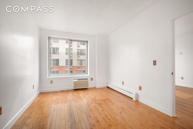 unfurnished room featuring a baseboard heating unit, light wood finished floors, baseboards, and an AC wall unit
