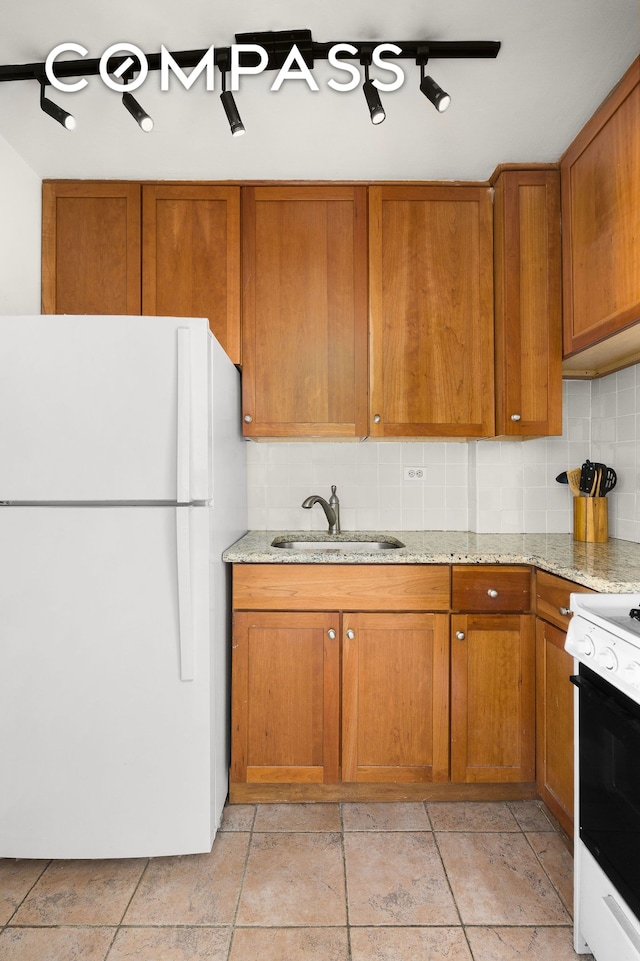 kitchen featuring brown cabinets, a sink, tasteful backsplash, freestanding refrigerator, and range