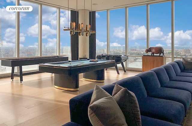 playroom featuring a city view, pool table, a wall of windows, wood finished floors, and a notable chandelier