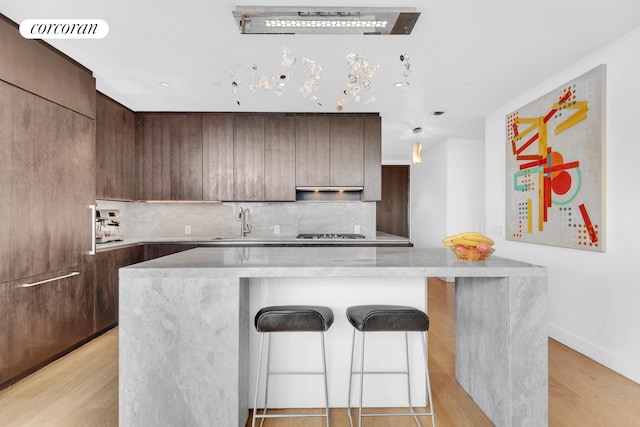 kitchen featuring decorative backsplash, a breakfast bar, a kitchen island, gas stovetop, and modern cabinets