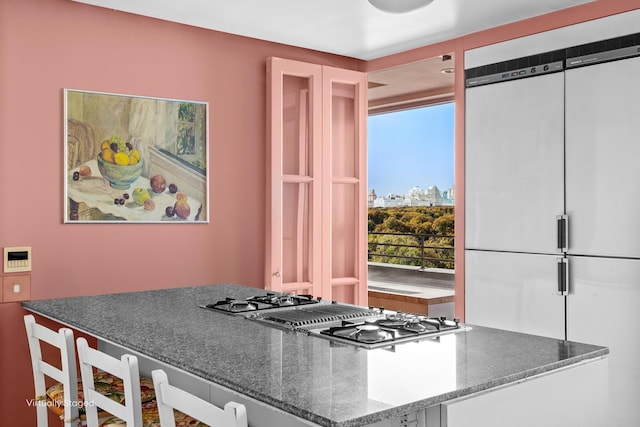 kitchen featuring dark stone counters, a view of city, built in fridge, and stainless steel gas cooktop